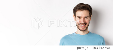 Close-up of handsome caucasian man smiling with white teeth, looking confident at camera, standing in blue shirt on white background Close-up of handsome caucasian man smiling with white teeth, looking confident at camera, standing in blue shirt on white background 103142758