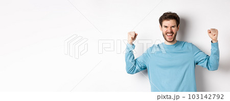 Portrait of satisfied handsome man winning prize, rejoicing in triumph, celebrating victory and shouting yes, standing over white background Portrait of satisfied handsome man winning prize, rejoicing in triumph, celebrating victory and shouting yes, standing over white background 103142792