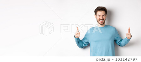 Cheerful young man showing thumbs up and smiling, recommend good product, praising choice, standing on white background 103142797