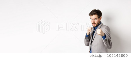 Serious man in suit raising hands in boxer pose, going to fight, looking confident, beckon to attack, standing on white background in defensive pose Serious man in suit raising hands in boxer pose, going to fight, looking confident, beckon to attack, standing on white background in defensive pose 103142809