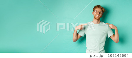 Confident redhead man in glasses and t-shirt, smiling with smug face and pointing at himself, bragging while standing over turquoise background Confident redhead man in glasses and t-shirt, smiling with smug face and pointing at himself, bragging while standing over turquoise background 103143694