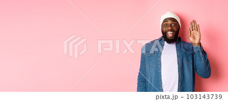 Friendly smiling Black man saying hello, waving hand, greeting you, standing over pink background 103143739