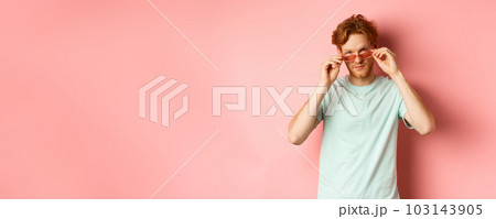 Handsome redhead man in summer sunglasses looking sassy at camera, standing over pink background 103143905