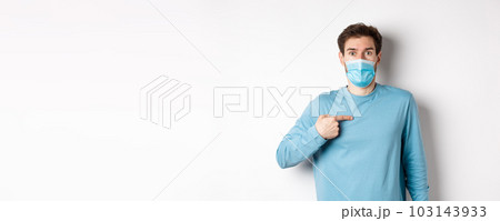 Coronavirus, health and quarantine concept. Surprised guy in medical mask points at himself, standing over white background Coronavirus, health and quarantine concept. Surprised guy in medical mask points at himself, standing over white background 103143933