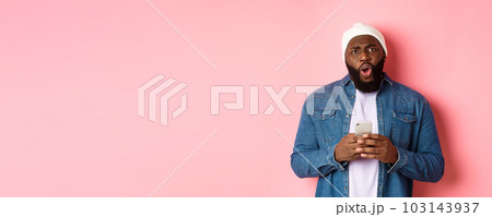 Technology and online shopping concept. Confused and disappointed african-american man complaining, holding mobile phone and staring at camera Technology and online shopping concept. Confused and disappointed african-american man complaining, holding mobile phone and staring at camera 103143937