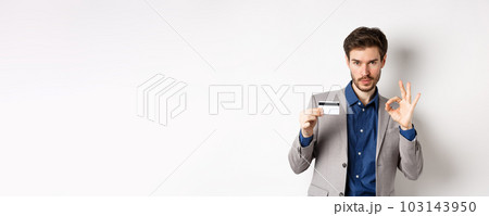 Happy male bank client in business suit showing plastic credit card and okay sign, smiling satisfied, standing on white background Happy male bank client in business suit showing plastic credit card and okay sign, smiling satisfied, standing on white background 103143950