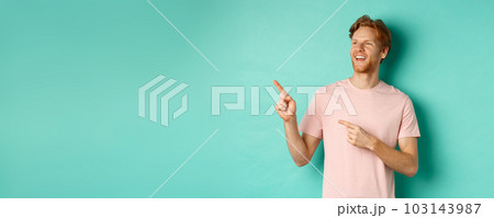 Dreamy handsome guy with red hair, smiling and looking at upper left corner with awe, admire something, standing over mint background 103143987