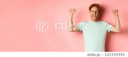 Happy winner with red hair and beard celebrating victory, shouting yes with joy and raising hands up, enjoy success, standing over pink background Happy winner with red hair and beard celebrating victory, shouting yes with joy and raising hands up, enjoy success, standing over pink background 103144395