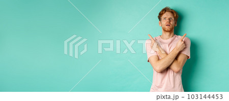 Confused young man in t-shirt looking up, pointing fingers sideways and feeling puzzled, cant decide, standing over turquoise background Confused young man in t-shirt looking up, pointing fingers sideways and feeling puzzled, cant decide, standing over turquoise background 103144453