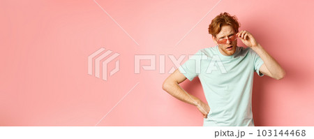 Tourism and vacation concept. Confused funny guy with red messy hair and beard, take-off glasses and frowning puzzled, standing over pink background 103144468
