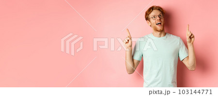 Amazed redhead guy in glasses checking out special deal, looking and pointing fingers up with amazed face, standing over pink background Amazed redhead guy in glasses checking out special deal, looking and pointing fingers up with amazed face, standing over pink background 103144771