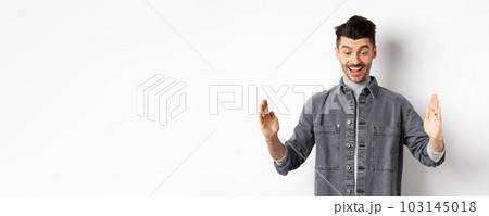 Excited caucasian man showing big size object, shaping large thing and smiling amazed, standing on white background Excited caucasian man showing big size object, shaping large thing and smiling amazed, standing on white background 103145018