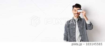 Happy handsome man with moustache show plastic credit card on eye, smiling excited at camera, standing on white background 103145565