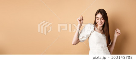 Carefree woman dancing and having fun, close eyes and smiling, standing on beige background 103145708