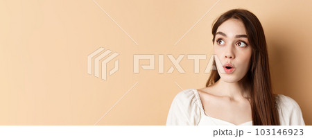 Close up portrait of excited pretty woman looking aside logo, say wow with amazed face, standing on beige background 103146923