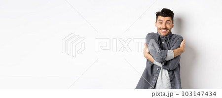 Happy handsome man hugging himself and smiling, embracing own body, standing on white background in grey jacket 103147434