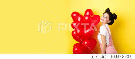 Valentines day and relationship concept. Fashionable asian woman posing near red hearts balloons, surprise for lover on special date, yellow background 103148503