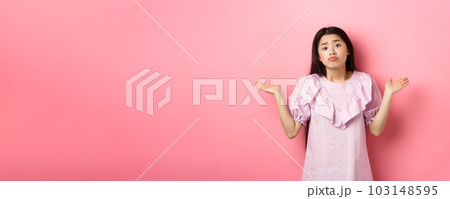 Sorry cant help. Clueless asian girl shrugging with sad face, know nothing, standing indecisive against pink background 103148595