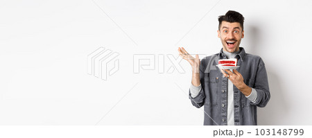 Excited man celebrating birthday, looking happy, holding cake with candle, making wish, standing happy against white background 103148799