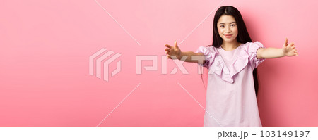 Cute teen asian girl stretch out hands for hug, want to cuddle, friendly greeting you, standing on pink background 103149197