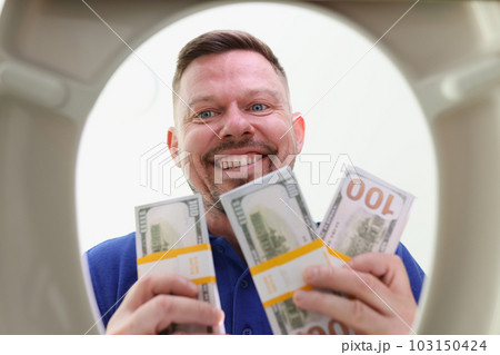 Smiling man looks into toilet bowl holding wads of dollars Smiling man looks into toilet bowl holding wads of dollars 103150424