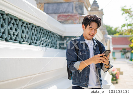 Portrait of Asian male traveler using a mobile phone on sidewalk of buddhist temple on street in Bangkok, Thailand, Southeast Asia - smart phone and internet for traveling concept Portrait of Asian male traveler using a mobile phone on sidewalk of buddhist temple on street in Bangkok, Thailand, Southeast Asia - smart phone and internet for traveling concept 103152153