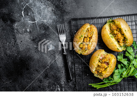 Turkish Kumpir, baked potatoes stuffed with cheese, bacon, salty cucumber, herbs and butter. Black background. Top view. Copy space Turkish Kumpir, baked potatoes stuffed with cheese, bacon, salty cucumber, herbs and butter. Black background. Top view. Copy space 103152638
