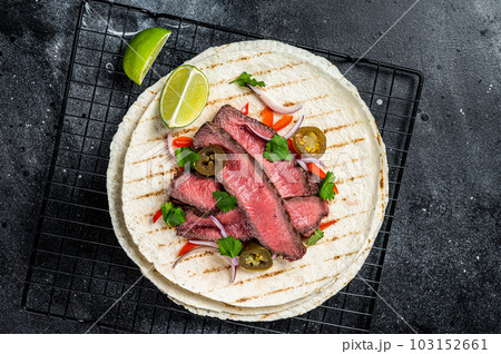 Grilled Beef steak Fajitas, taco tortillas with onion, jalapeno and bell pepper. Black background. top view 103152661
