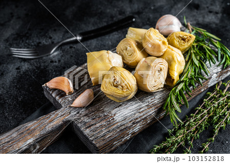 Artichokes hearts marinated with olive oil and herbs, pickled artichoke with garlic on wooden board. Black background. Top view Artichokes hearts marinated with olive oil and herbs, pickled artichoke with garlic on wooden board. Black background. Top view 103152818
