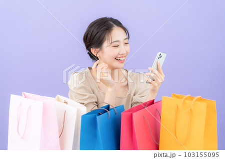 パープルバックでショッピングをして買い物袋を並べてスマホを操作する若い女性 103155095