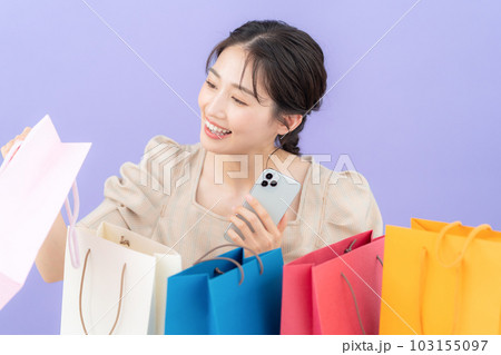 パープルバックでショッピングをして買い物袋を並べてスマホを操作する若い女性 103155097