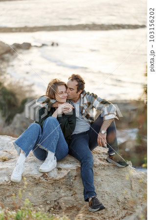 Portrait of a middle-aged couple sitting on a rock at the beach in Cyprus. They are wearing casual clothes 103156202