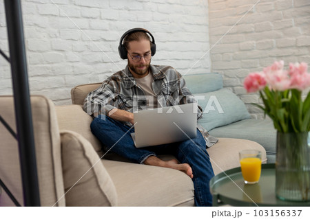 Man gamer playing on laptop on cough, having online network game, using headphones and microphone Man gamer playing on laptop on cough, having online network game, using headphones and microphone 103156337