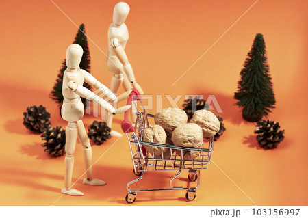 Couple of dummies pushing shopping cart with nuts next to pine trees on orange background 103156997