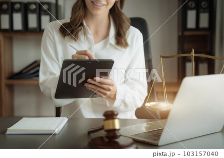 Justice and law concept.Female judge in a courtroom the gavel, working with digital tablet computer on wood table in sun light. 103157040