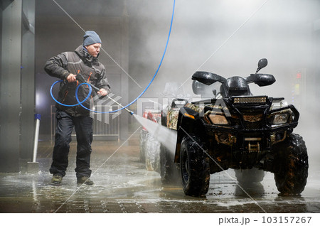 Full length of man cleaning quad bike with high pressure water sprayer at self-service car washing station 103157267