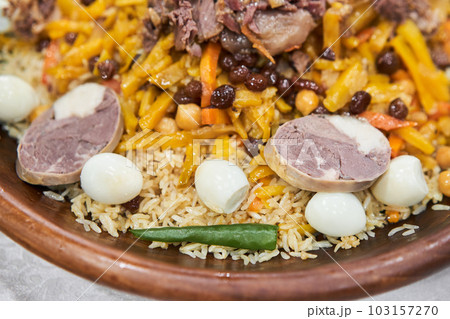 A traditional Uzbek dish called pilaf. Rice with meat, carrots, onions, quail eggs and kazy in a plate of astau on the table. A portion for three people. Close up  103157270