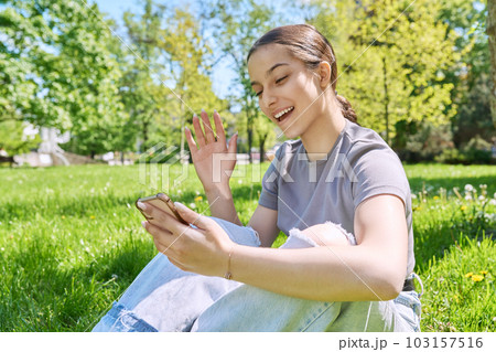 Teenage girl in park on grass using smartphone for online meeting 103157516