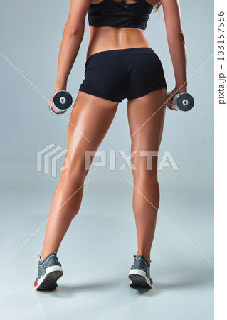 Athletic woman pumping up muscles with dumbbells on gray background 103157556