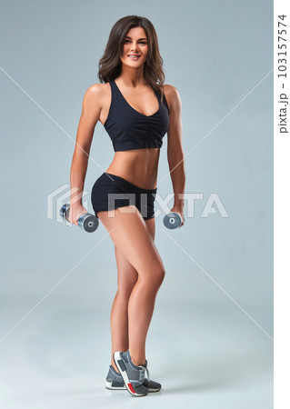 Athletic woman pumping up muscles with dumbbells on gray background Athletic woman pumping up muscles with dumbbells on gray background 103157574