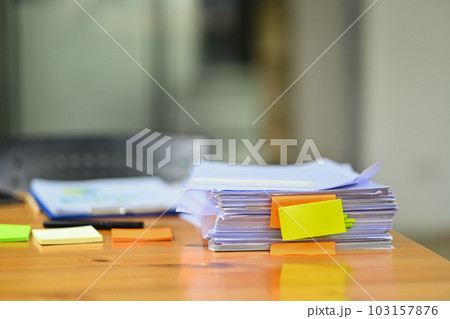 Pile of documents with colorful sticky notes on wooden office desk. Organized document management system concept 103157876