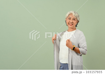 Positive gray haired senior woman posing over green pastel background and smiling to camera 103157935