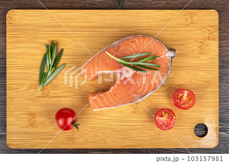 Top view of raw salmon or trout steak, with rosemary and cherry tomatoes on a cutting board. Top view of raw salmon or trout steak, with rosemary and cherry tomatoes on a cutting board. 103157981