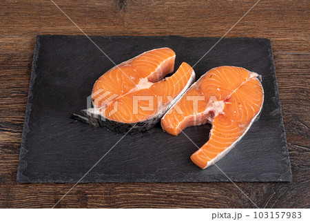 Raw salmon steaks on stone serving board over wooden background. 103157983