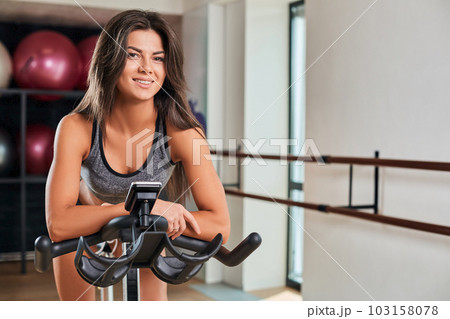 Muscular young woman working out on the exercise bike at the gym, intense cardio workout. Muscular young woman working out on the exercise bike at the gym, intense cardio workout. 103158078