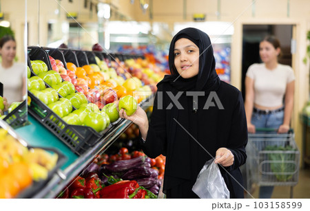 Asian girl in hijab buys ripe apples in supermarket 103158599
