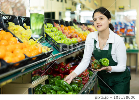 Asian female seller in apron chooses ripe bell pepper Asian female seller in apron chooses ripe bell pepper 103158600