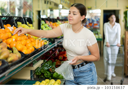 Happy smiling woman making purchases in supermarket, choosing fresh tangerines 103158637