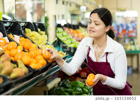 Female grocery store worker lays out ripe tangerines on counter and display case 103158652