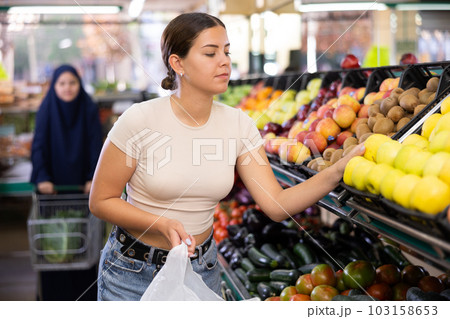 Happy smiling woman making purchases in supermarket, choosing fresh apples 103158653